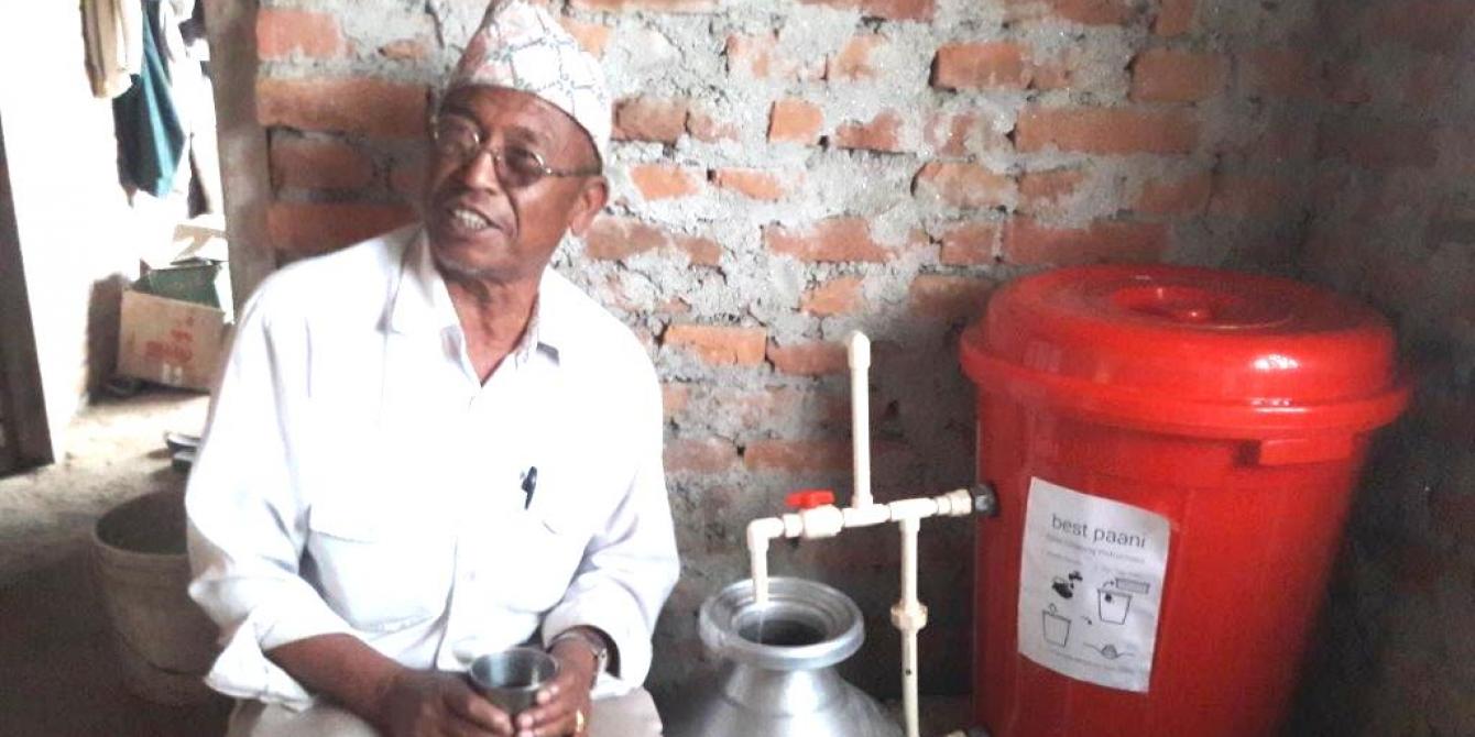 Harka Bahadur Ghimire holding a glass of filtered water. Photo by: Oxfam